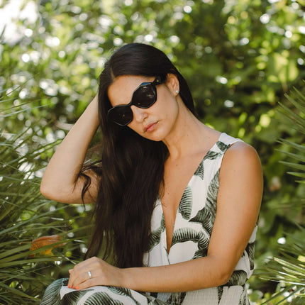 Mujer con gafas de sol Hanukeii® Moorea Black / Black sentada entre plantas verdes.