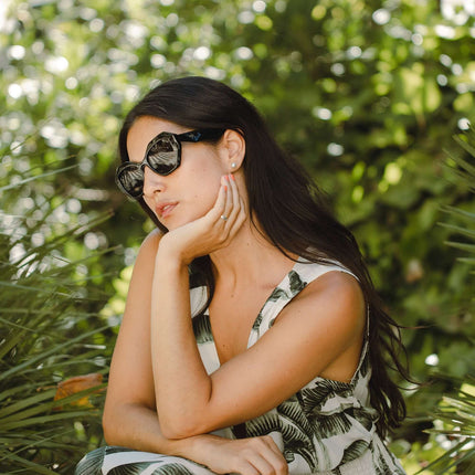 Mujer usando gafas de sol Hanukeii® Moorea Black / Black en un entorno natural con plantas.