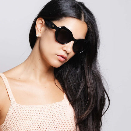 Mujer usando gafas de sol Hanukeii® Moorea Black / Black con peinado largo y piel clara.