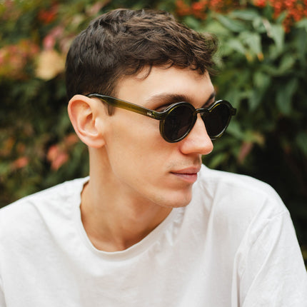 Joven usando gafas de sol Hanukeii® Harbor Green / Black en un entorno natural, resaltando su estilo y calidad.